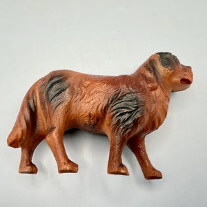 May include: A molded dog figurine featuring a textured brown coat with dark black patches on the back and ears. The canine figure is depicted in a standing position with a slightly open mouth, showcasing detailed fur patterns and a solid, sturdy build.