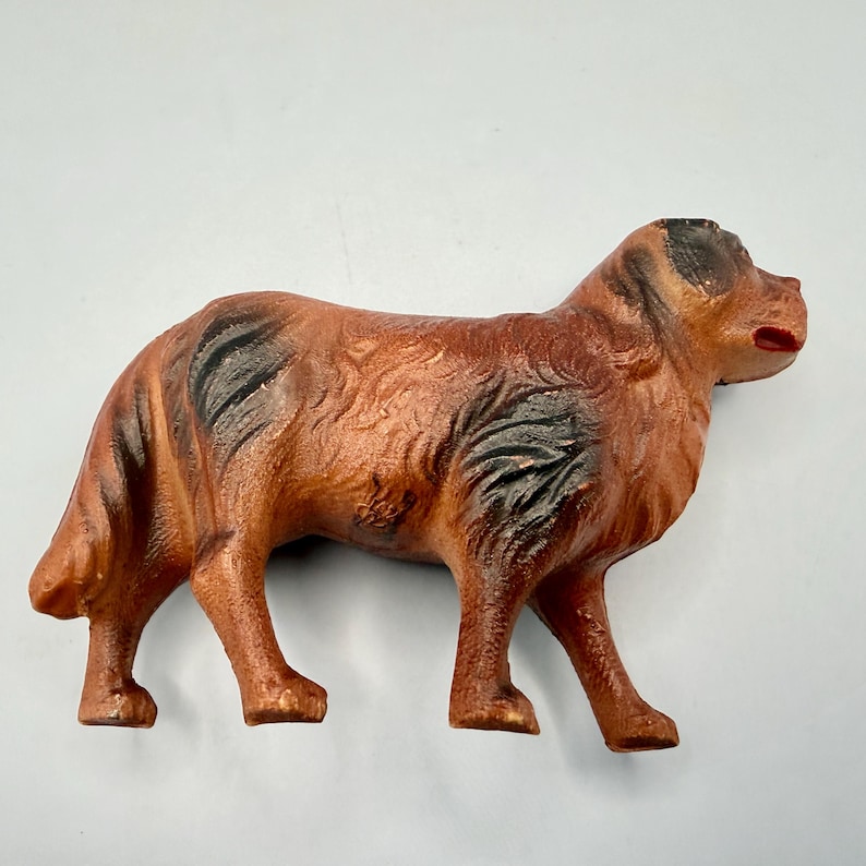 May include: A molded dog figurine featuring a textured brown coat with dark black patches on the back and ears. The canine figure is depicted in a standing position with a slightly open mouth, showcasing detailed fur patterns and a solid, sturdy build.
