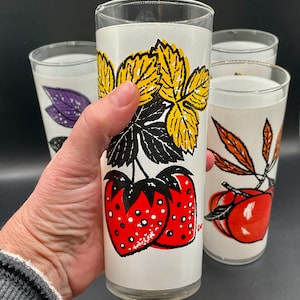 Four vintage drinking glasses with a white background and colorful fruit and leaf designs. The glasses feature strawberries, leaves, and a yellow flower design.