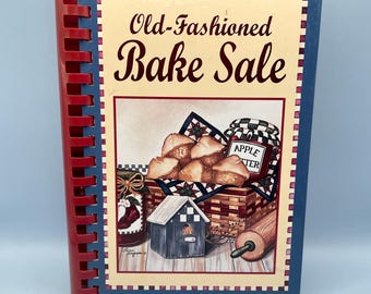 Puede incluir: Un libro de cocina con espiral titulado "Old-Fashioned Bake Sale". La portada presenta ilustraciones de productos horneados, una cesta, un tarro de mantequilla de manzana y un rodillo. La encuadernación es roja y la portada tiene un borde azul.