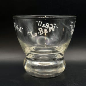 May include: Clear glass bowl with a thick base. The bowl has "It's a "Lo-Ball" " etched on the side.