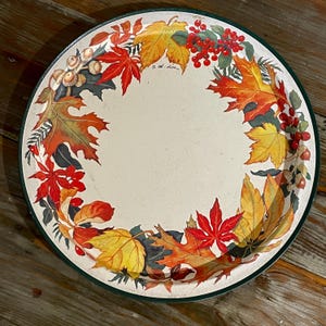 Puede incluir: Bandeja redonda para servir con centro crema y borde verde. La bandeja está decorada con un colorido diseño de hojas y bayas otoñales. Las hojas son en tonos rojos, naranjas y amarillos. Diámetro aproximado de 30 cm.