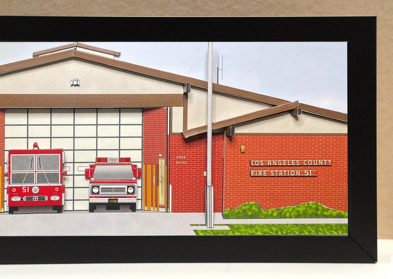 May include: A paper model of a Los Angeles County Fire Station 51, with two red fire trucks parked inside the bay. The building is made of red brick with a brown roof and a sign that reads "Los Angeles County Fire Station 51".