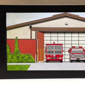 May include: A red fire truck with the number 51 on the side is parked in a fire station bay. The fire station is a paper model with a brown roof and red brick walls. There is a green bush in front of the fire station.