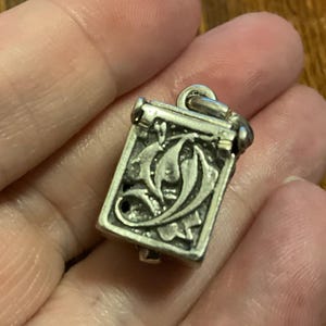 以下が含まれることがあります： 小さな装飾的な箱の形をした銀製のチャーム。蓋はヒンジで開閉します。箱は花柄で飾られています。