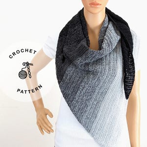 May include: A crocheted shawl in a gradient of gray and black, draped on a mannequin. The shawl's design features a triangular shape with a textured stitch pattern. The image includes a logo that says "CROCHET PATTERN".