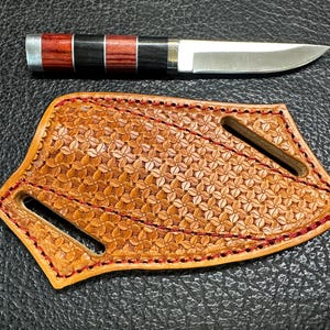 May include: A brown leather knife sheath with a floral pattern and red stitching. The sheath has a single slot for a knife blade.