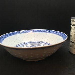 May include: A white ceramic bowl with a blue and white pattern. The bowl has a round shape and a wide rim. The pattern includes a repeating design of flowers and leaves.
