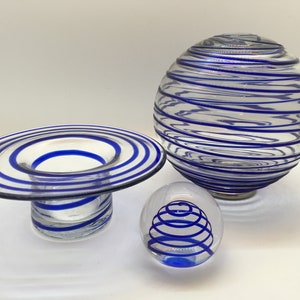 Puede incluir: Tres cuencos de vidrio con diseños en espiral azul. El cuenco más grande es una esfera, el cuenco mediano es un cuenco ancho y poco profundo, y el cuenco más pequeño es una esfera.