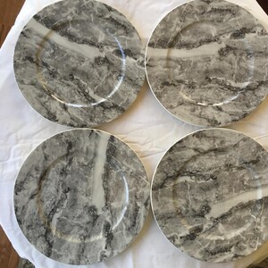 May include: Set of four gray and white marble charger plates. The plates have a decorative design that resembles marble.