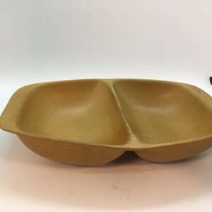 May include: A divided serving dish made of brown stoneware. The dish has two rounded sections.