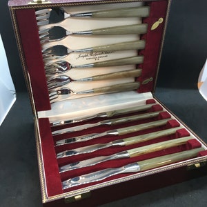 May include: A red velvet box with a gold latch, containing a set of six silver forks and six silver knives with brown handles. The box is labeled "Joseph Rodgers & Sons, Sheffield England".