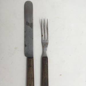 Op de afbeelding: Een vintage bestekset met houten handvatten. Het mes heeft een zilveren blad en de vork heeft vier tanden.