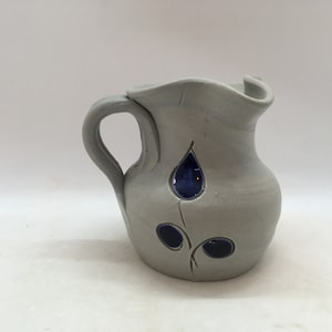 May include: A gray ceramic pitcher with a blue floral design. The pitcher has a wide mouth and a handle.