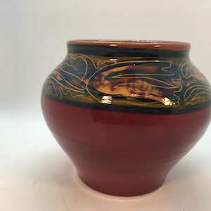 Pode incluir: Um vaso de cerâmica vermelho com um design decorativo de linhas e cores em espiral em tons de azul, verde, amarelo e laranja.