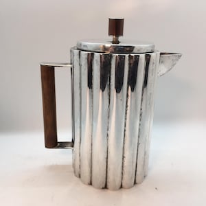 May include: A silver pitcher with a wooden handle and a fluted design. The pitcher has a lid with a wooden knob.