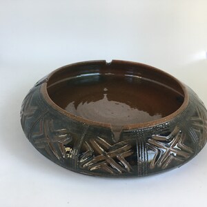 May include: A brown ceramic ashtray with a dark brown glaze and a geometric pattern around the rim.