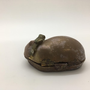 May include: A small, antique brass box with a hinged lid. The box has a rounded, oval shape and a tarnished, aged appearance. A decorative clasp and handle are visible on the top. The box is likely used for storing small items.