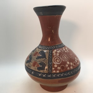 May include: A decorative ceramic vase with a brown body, black rim, and base. The vase features painted floral and spiral designs in blue, white, and brown. The vase is approximately 8 inches tall.