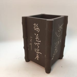 May include: A square, dark brown ceramic planter with a bamboo design and Chinese characters. The characters read "海  老  古  董  茶  壺".