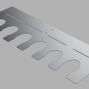 May include: A silver-colored metal plate with multiple U-shaped cutouts along one edge. The plate has several small holes and straight cut lines. The design appears to be for a specific purpose, possibly for organizing or holding items.