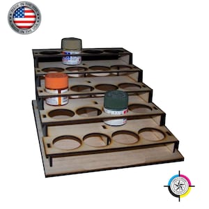 May include: A wooden paint rack with five tiers, each tier has six circular holes for holding paint bottles. The rack is made of light brown wood and has a natural finish. There are three paint bottles on the rack, one green, one orange, and one tan.
