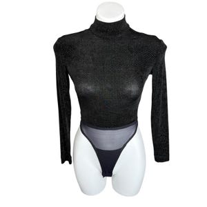 May include: Black bodysuit with long sleeves and a high neckline. The top is covered in small, sparkling embellishments. The bottom portion features a sheer mesh panel and a thong cut. The garment is displayed on a white mannequin.