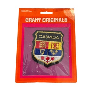 May include: A Canada patch with a shield design, featuring the word "CANADA" in white. The patch is in a clear plastic package with a pink and orange cardboard backing. The package reads "GRANT ORIGINALS".