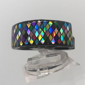 Può includere: Un anello nero con un motivo a rombi colorati. I diamanti sono iridescenti e riflettono la luce in diversi colori.