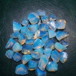 Pode incluir: Um monte de pequenas pedras de opala azul e branca iridescentes. As pedras têm uma forma irregular e uma aparência translúcida.