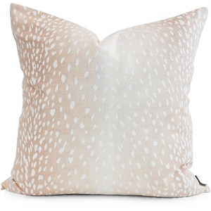Könnte beinhalten: Quadratisches Zierkissen mit einem beige-weißen Fleckenmuster. Das Kissen hat einen hellbraunen Hintergrund mit weißen Flecken, wodurch ein gesprenkelter Effekt entsteht. Es besteht aus einem weichen Stoff und ist für die Inneneinrichtung gedacht.