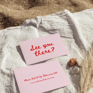 May include: Two pink cards with red text. The top card says "See you there?" and the bottom card says "Please RSVP by February 15th www.weddingwebsite.com/rsvp"