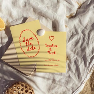 May include: A yellow card with red text that says "Save the date" and a red heart. Below the heart is the text "Caroline & Nick" with a date and location.