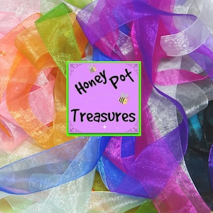 May include: A pile of colourful sheer ribbon in various shades of pink, blue, green, orange, and purple. The ribbon is arranged in a random pattern and has a shimmery finish. The text "Honey Pot Treasures" is visible on a pink and green label.