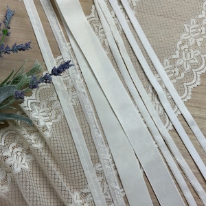 May include: A collection of white ribbon trims, including lace, satin, and grosgrain, arranged on a white lace fabric background.