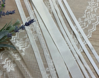 May include: A collection of white ribbon trims, including lace, satin, and grosgrain, arranged on a white lace fabric background.