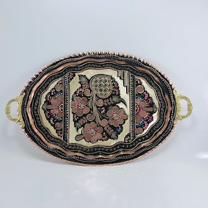 Puede incluir: Una bandeja de servir ovalada de cobre con un diseño floral en blanco y negro. La bandeja tiene dos asas de latón y un borde de cobre.