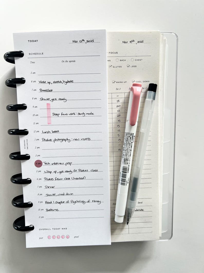Op de afbeelding: Een open planner met een schema voor 12 november 2025 en een focusgedeelte voor 4 november 2025. Een roze markeerstift markeert een tijdvak. Een roze en een zwarte pen liggen naast de planner.
