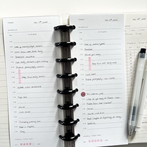 Op de afbeelding: Een planner met een zwarte binding, opengeklapt op twee pagina's met dagschema's. De linkerpagina is gedateerd 11 november 2025, de rechterpagina 12 november 2025. Elke pagina heeft een gedetailleerd schema.