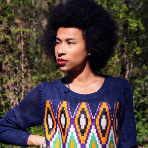 May include: A navy blue jumper featuring a geometric design in orange, purple, green, and white. The jumper has a round neck and long sleeves. The person in the image is wearing the jumper.