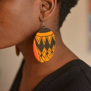 May include: A pair of large, round earrings with a geometric pattern in black, yellow, and red. The earrings are made of fabric and have a circular shape.