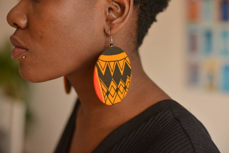 May include: A pair of large, round earrings with a geometric pattern in black, yellow, and red. The earrings are made of fabric and have a circular shape.