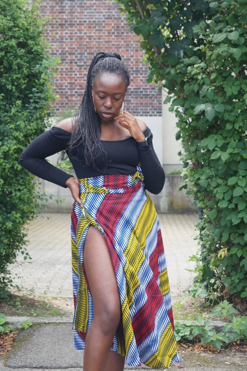 May include: A black off-the-shoulder top and a colourful wrap skirt. The skirt has a striking pattern of red, yellow, and blue stripes. The skirt features a high slit, adding a fashionable touch to the ensemble.