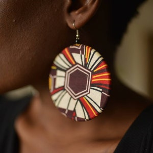May include: Large round earrings with a colorful geometric pattern in shades of red, yellow, white, and brown.