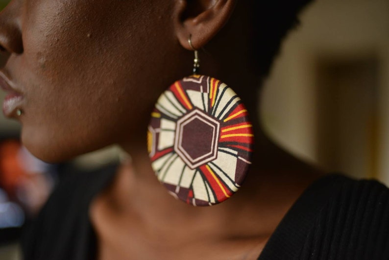 May include: Large round earrings with a colorful geometric pattern in shades of red, yellow, white, and brown.