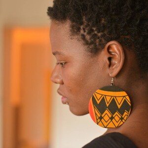 May include: A woman with short, dark hair wearing large, round earrings with a black, orange, and yellow geometric pattern.