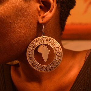 May include: Silver hoop earrings with a cutout of the continent of Africa. The earrings have a detailed, ornate design.