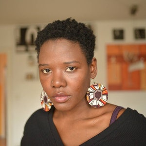 May include: A woman with short, dark hair wearing a black shirt and large, round, colorful earrings.
