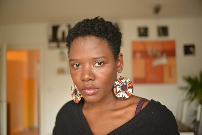May include: A woman with short, dark hair wearing a black shirt and large, round, colorful earrings.
