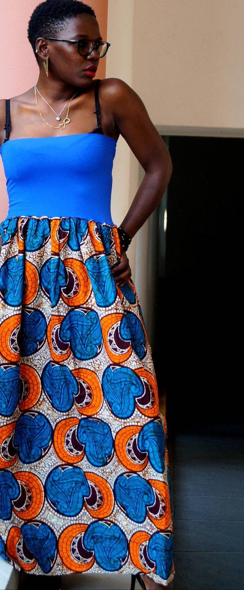 K&ouml;nnte beinhalten: Ein blaues Oberteil mit einem lebendigen, gemusterten Rock. Der Rock hat ein sich wiederholendes Design in Blau-, Orange- und Wei&szlig;t&ouml;nen. Der Look ist ein mutiges und farbenfrohes Mode-Statement.